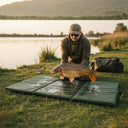 Un pêcheur à genoux manipulant avec précaution une carpe miroir au-dessus d'un tapis de réception de pêche No-Kill humide, au bord d'un lac.