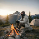 Homme portant un tour de cou polaire modèle 720 PROS Wear noir remonté sur le visage pour se protéger du froid lors d'un bivouac en montagne devant un feu de camp